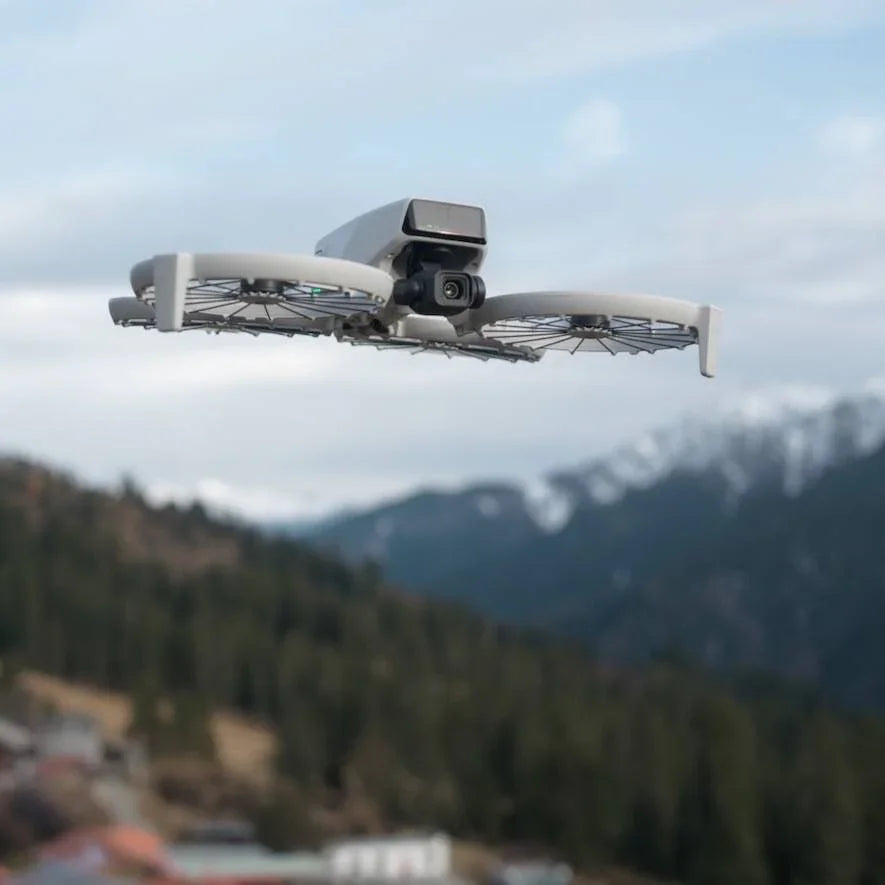DJI FPV drone flying outdoors with mountains and forest in the background under a cloudy sky