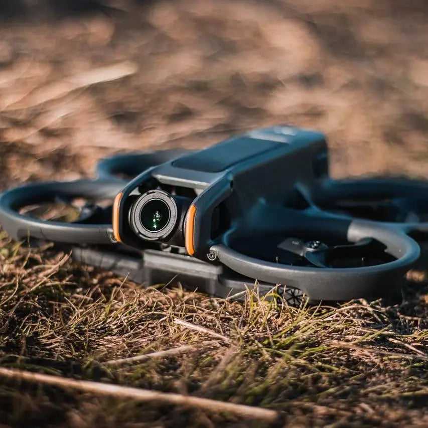 Compact black drone with camera resting on dry grass outdoors