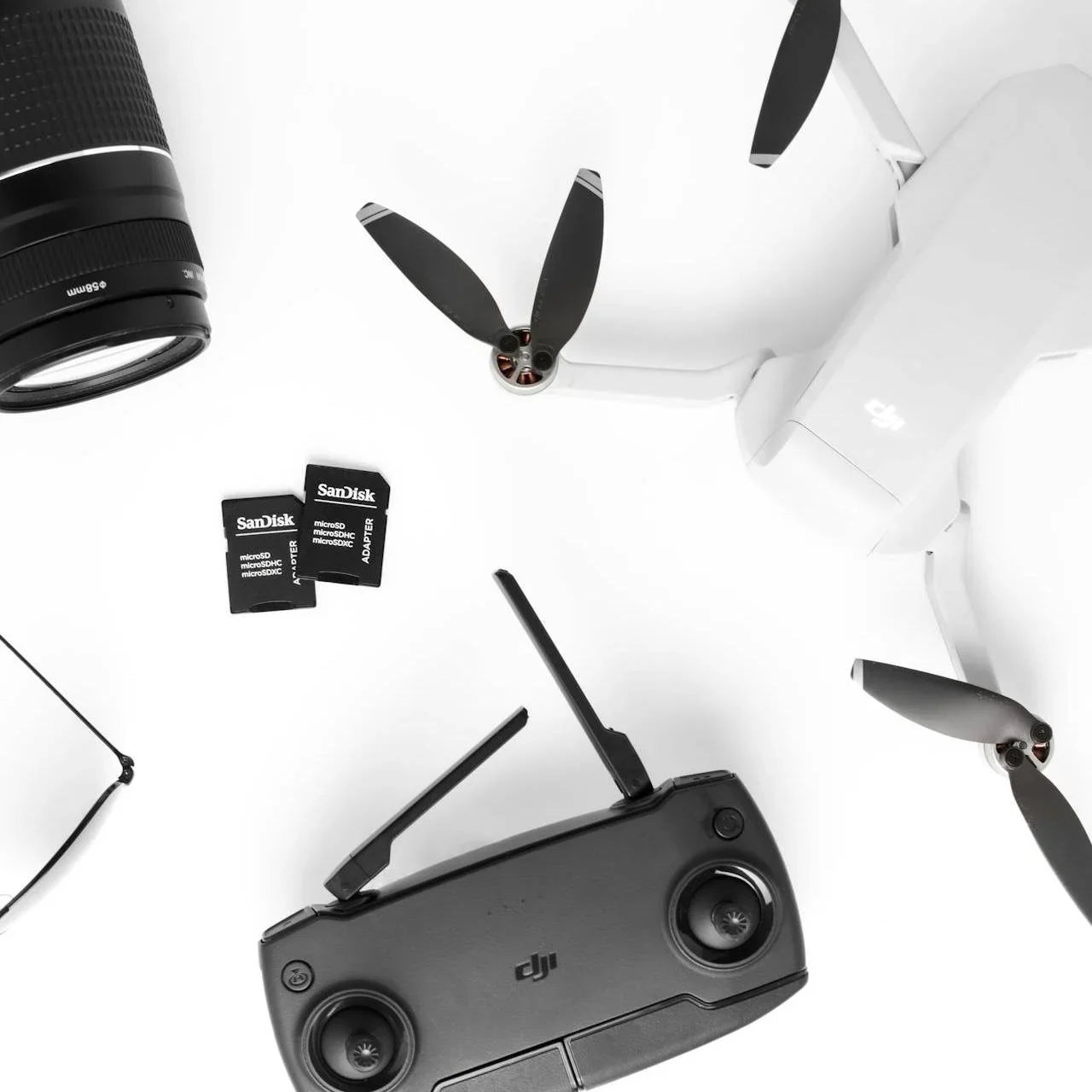 White DJI drone with propellers, black DJI remote, two SanDisk microSD adapters, and camera lens on white background